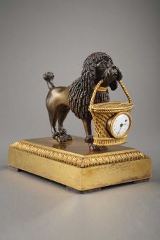 Adorable et rarissime pendulette d'époque Empire en bronze doré et patiné. Représentant un caniche tenant dans sa gueule un panier, dans lequel s'inscrit le cadran.