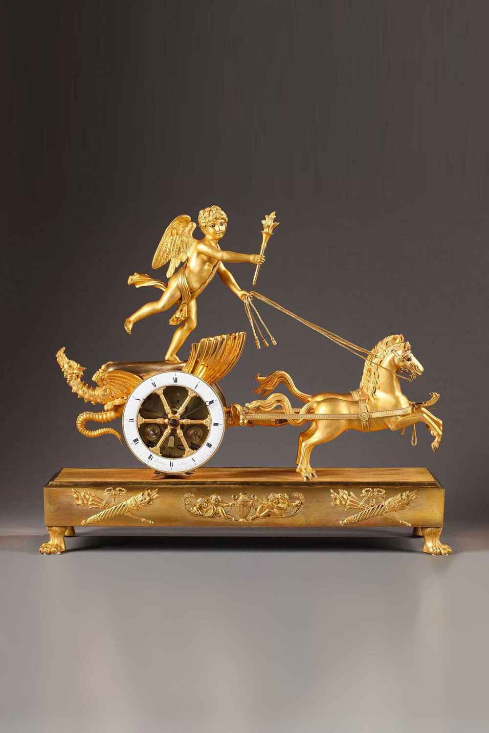 Pendule char en bronze doré et ciselé d'époque Directoire. Cupidon (aux yeux en émail) debout sur son char coquille tient les rennes de ses deux chevaux (yeux en émail).