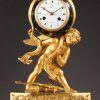 Pendule en bronze doré, ciselé et patine bleue d'époque Empire. Cupidon, dont le carquois et l'arc sont à ses pieds, maintient la voute céleste sur son épaule.